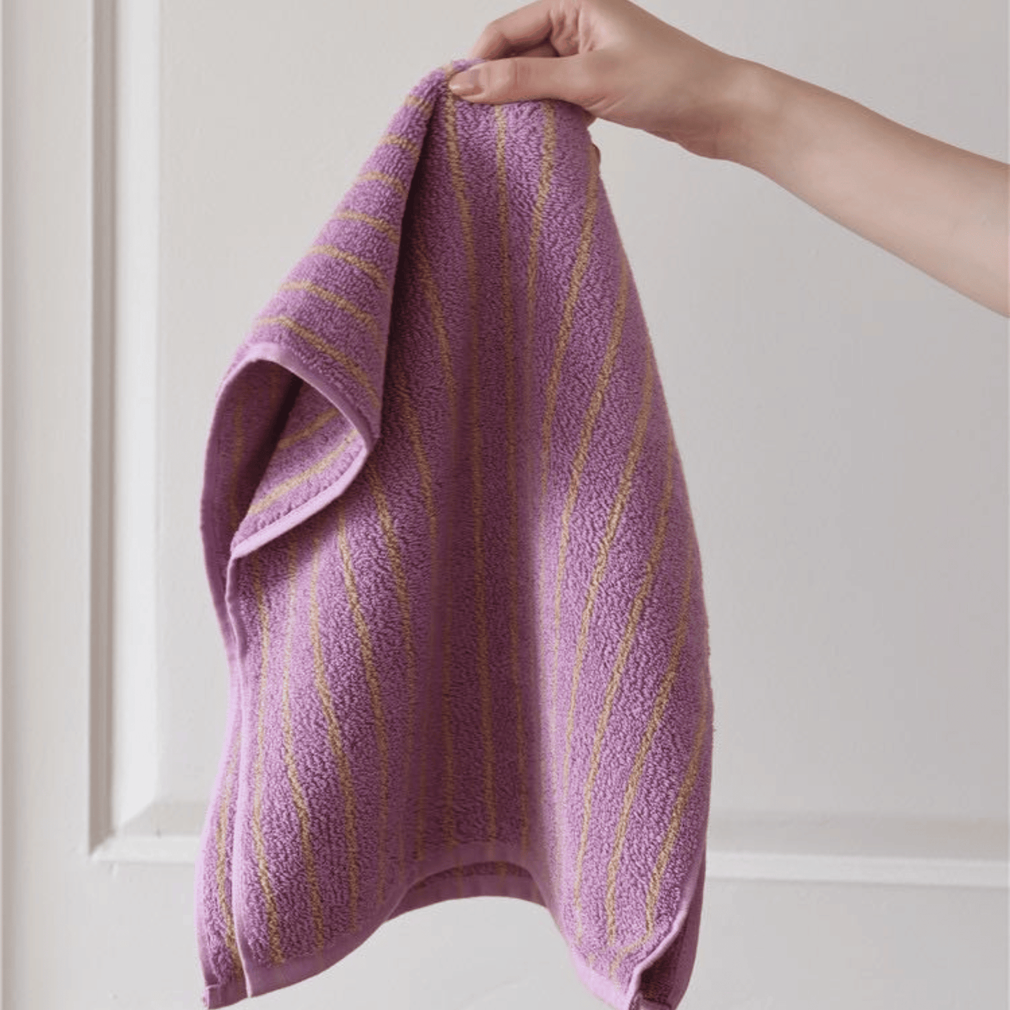 Purple towel with gold stripes held by a hand against a neutral background
