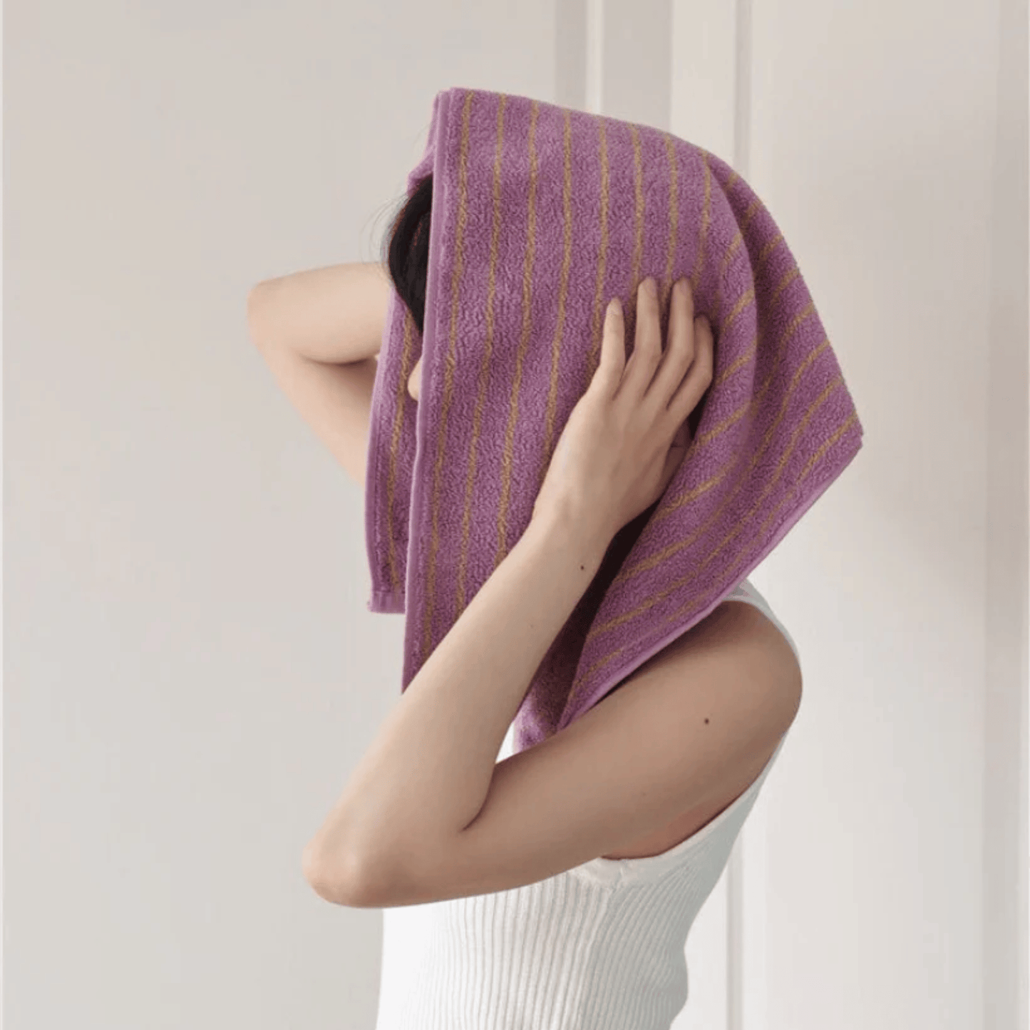 Person holding a purple towel over their head against a plain background