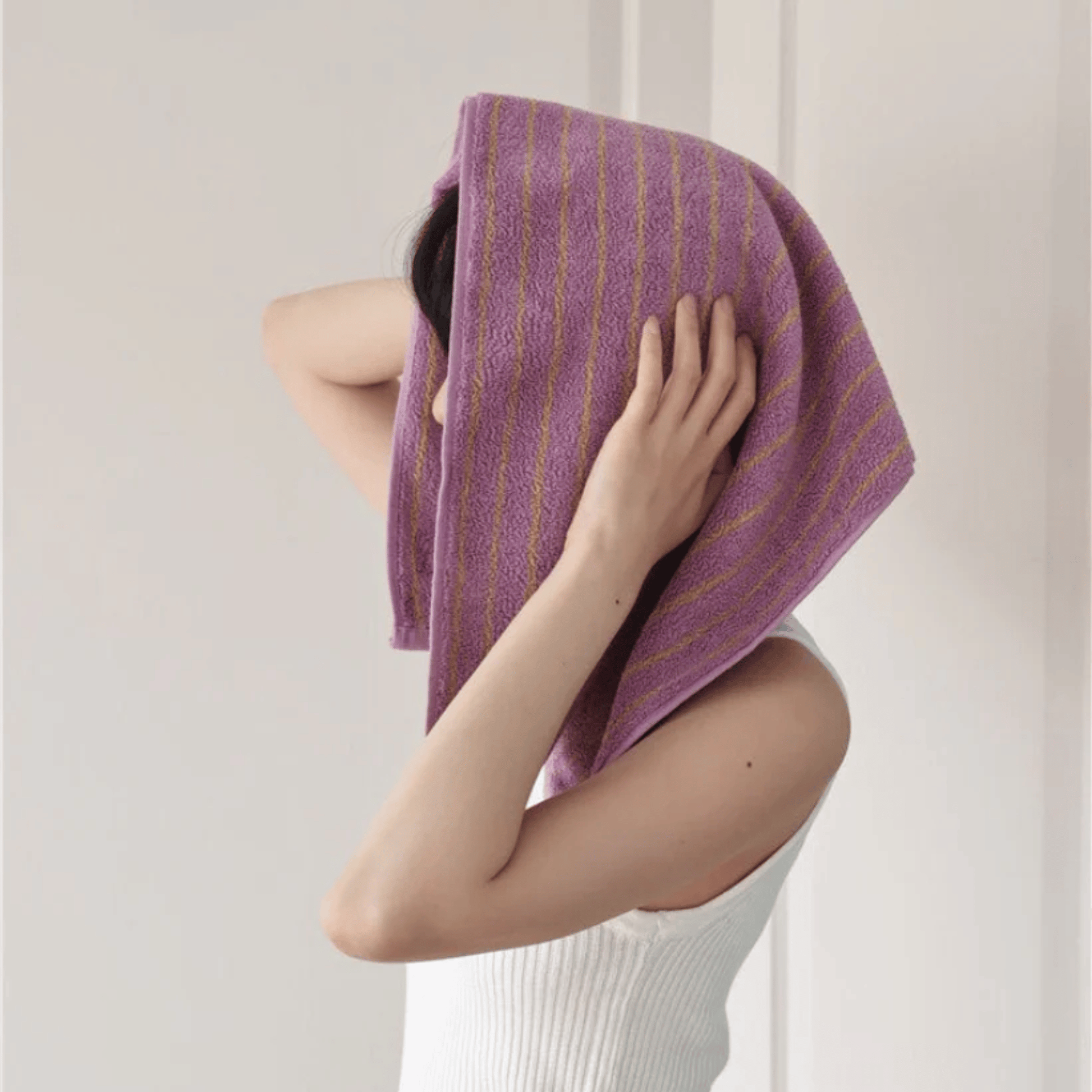 Person holding a purple towel over their head against a plain background