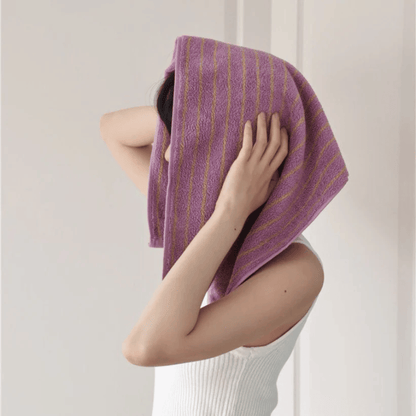Person holding a purple towel over their head against a plain background