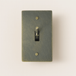Textured green light switch with a gold toggle on a beige background
