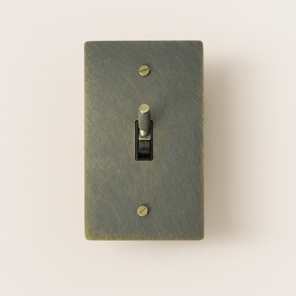 Textured green light switch with a gold toggle on a beige background