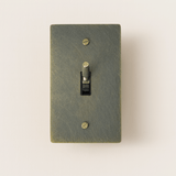 Textured green light switch with a gold toggle on a beige background