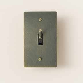 Textured green light switch with a gold toggle on a beige background
