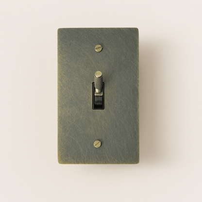 Textured green light switch with a gold toggle on a beige background