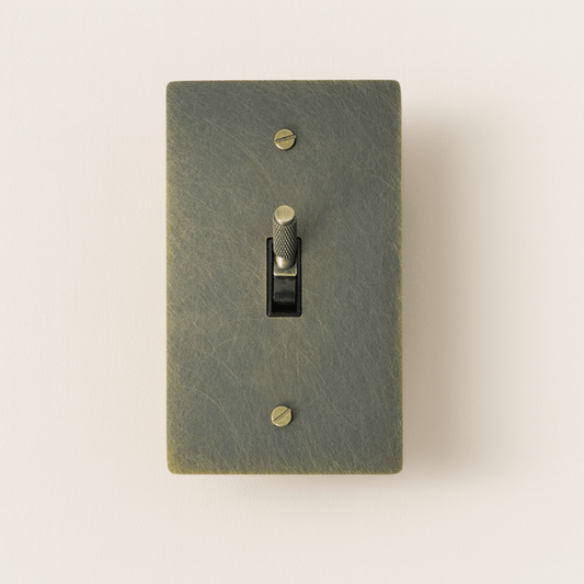 Textured green light switch with a gold toggle on a beige background