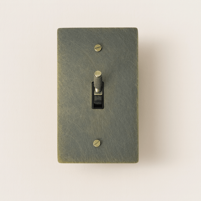 Textured green light switch with a gold toggle on a beige background