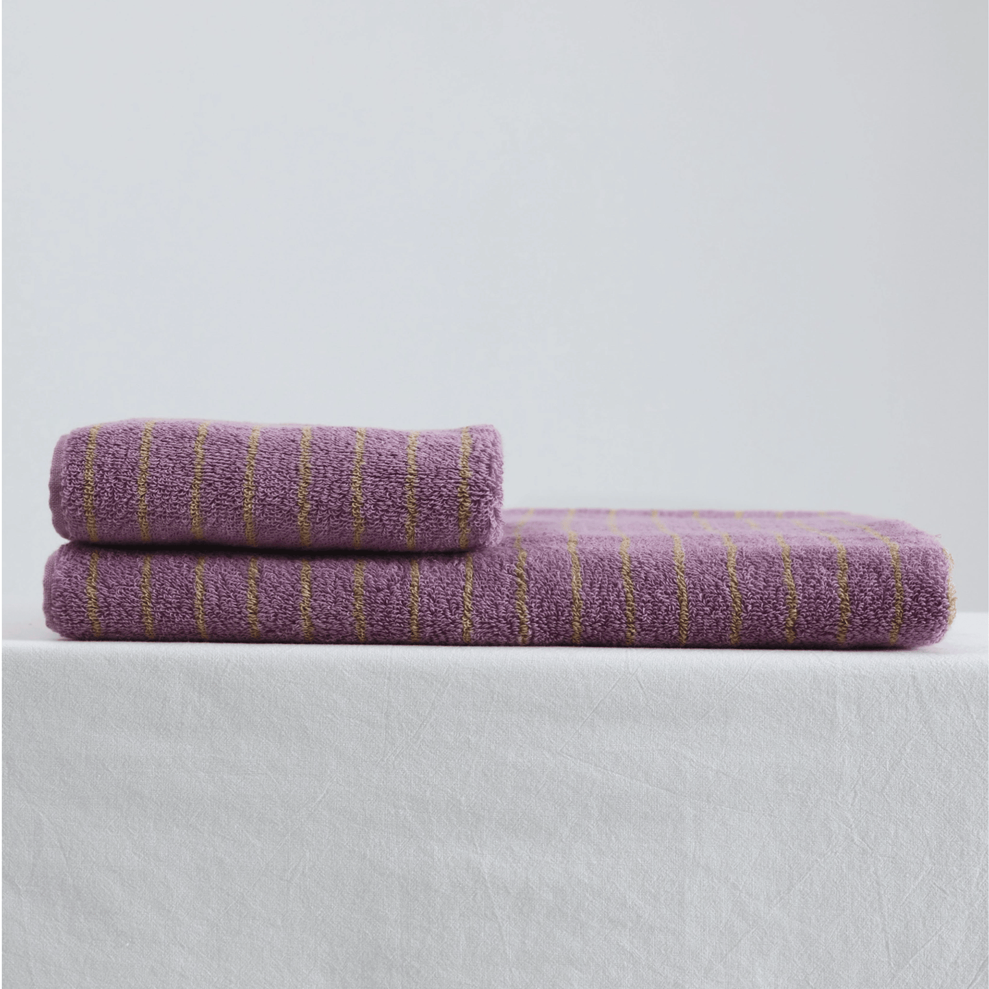 Two purple towels with gold stripes on a light gray background