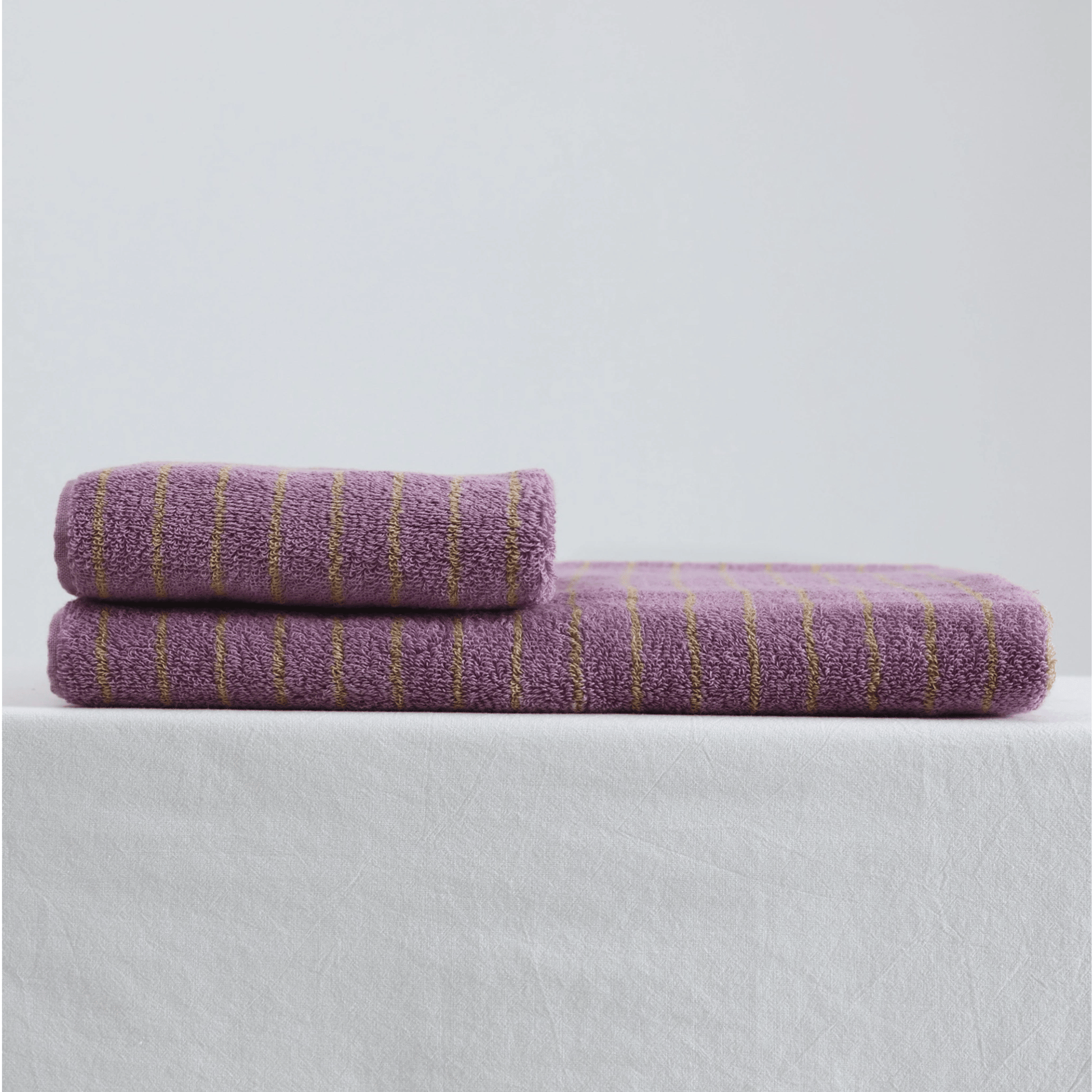 Two purple towels with gold stripes on a light gray background