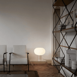Modern living room with white armchair, glass coffee table, and geometric shelf.
