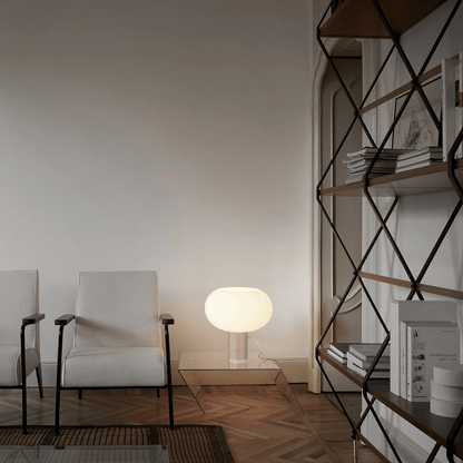 Modern living room with white armchair, glass coffee table, and geometric shelf.