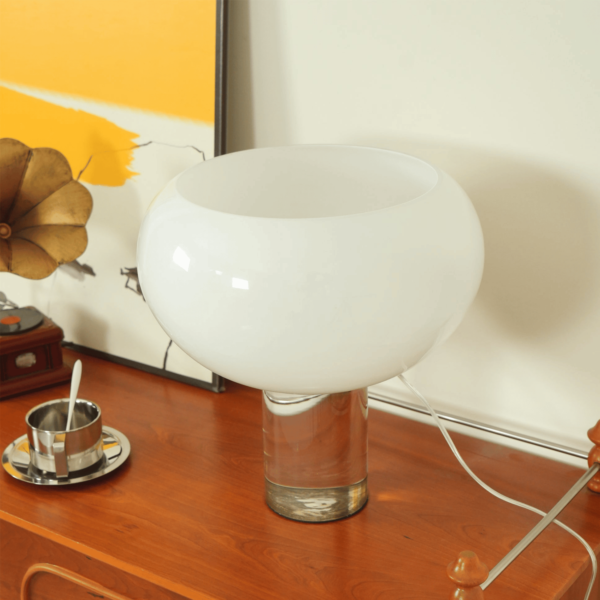 White glass table lamp on a wooden surface with a vintage gramophone in the background.