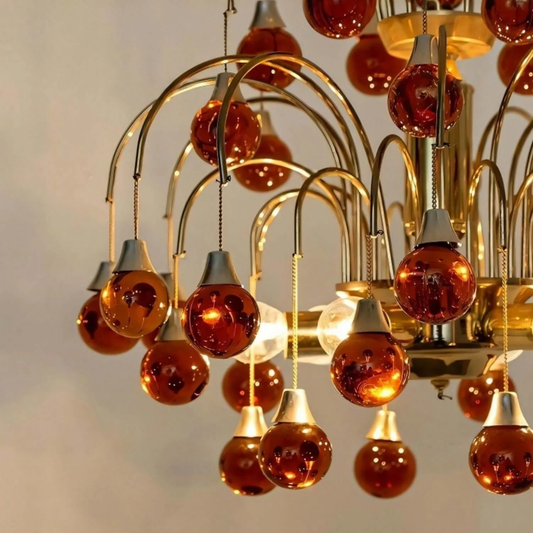 Chandelier with orange glass bulbs and gold metal structure against a neutral background