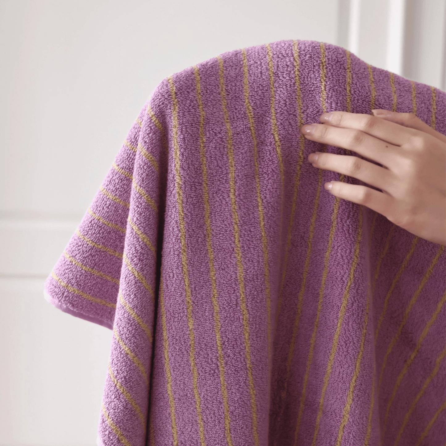 Purple towel with yellow stripes held by a hand against a white background
