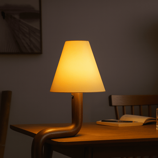 Table lamp with a warm glow on a wooden table against a dark wall.