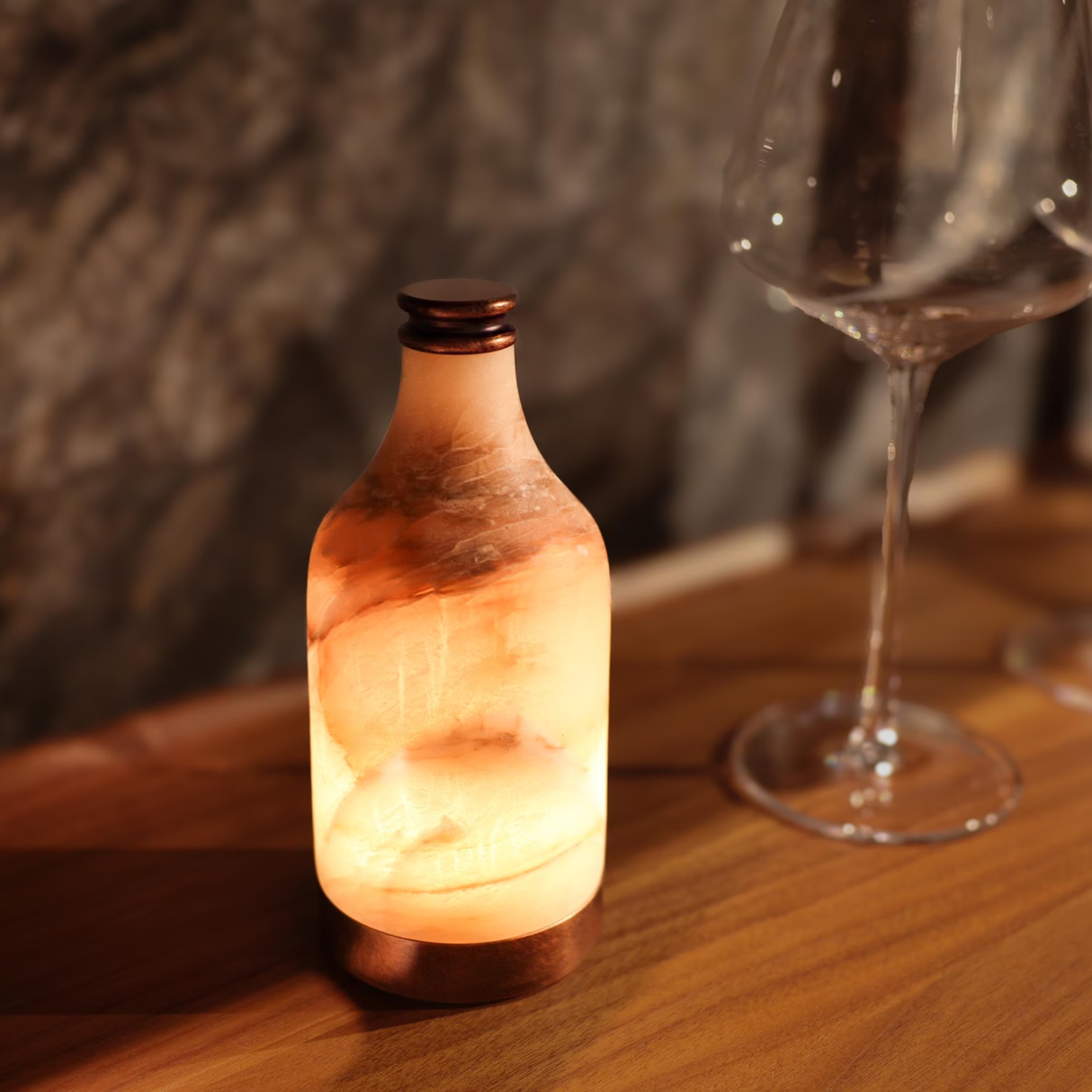 Decorative bottle lamp on a wooden surface with a blurred glass in the background