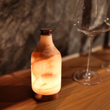 Decorative bottle lamp on a wooden surface with a blurred glass in the background