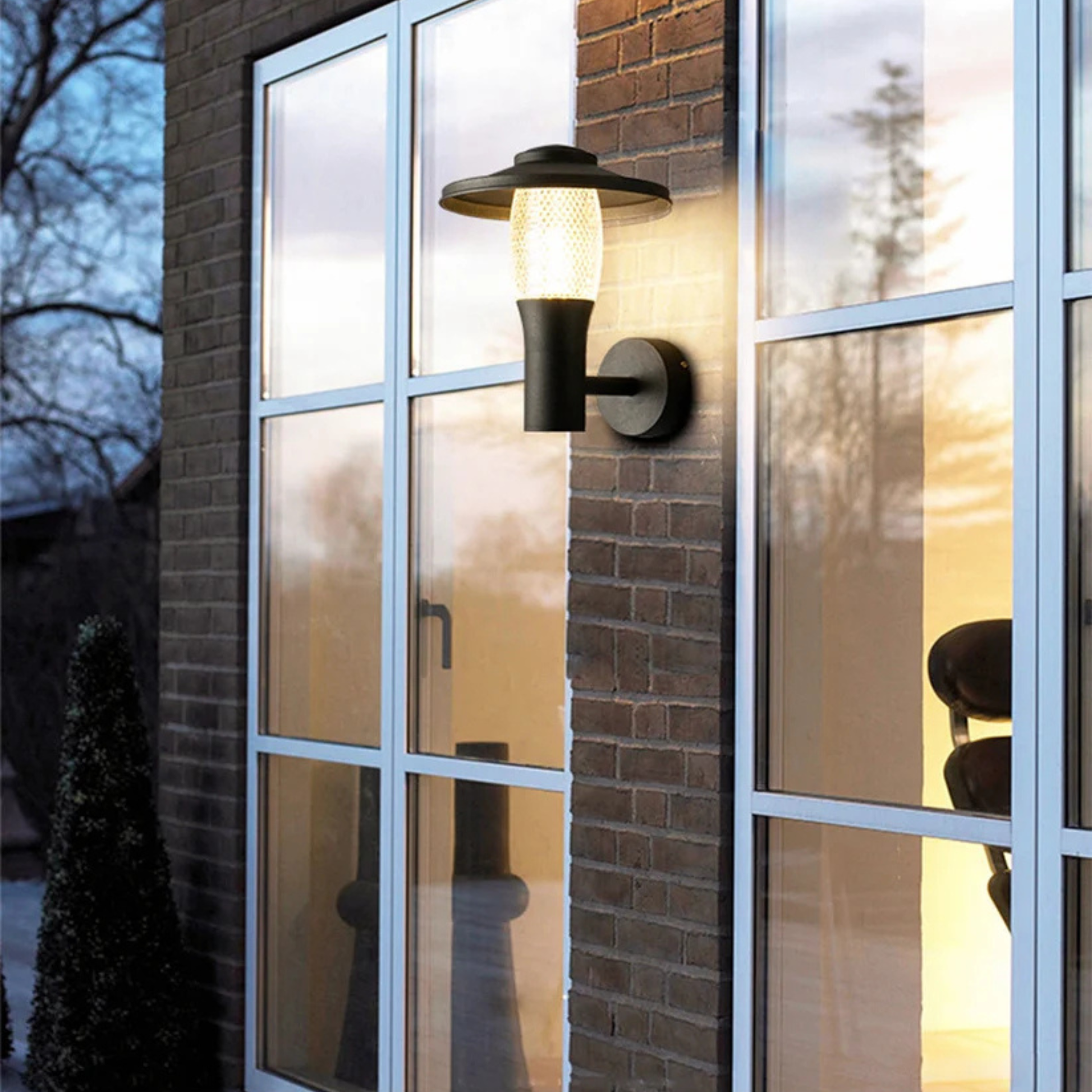 Elegant glass-walled exterior reflecting soft light from a modern outdoor wall sconce at dusk