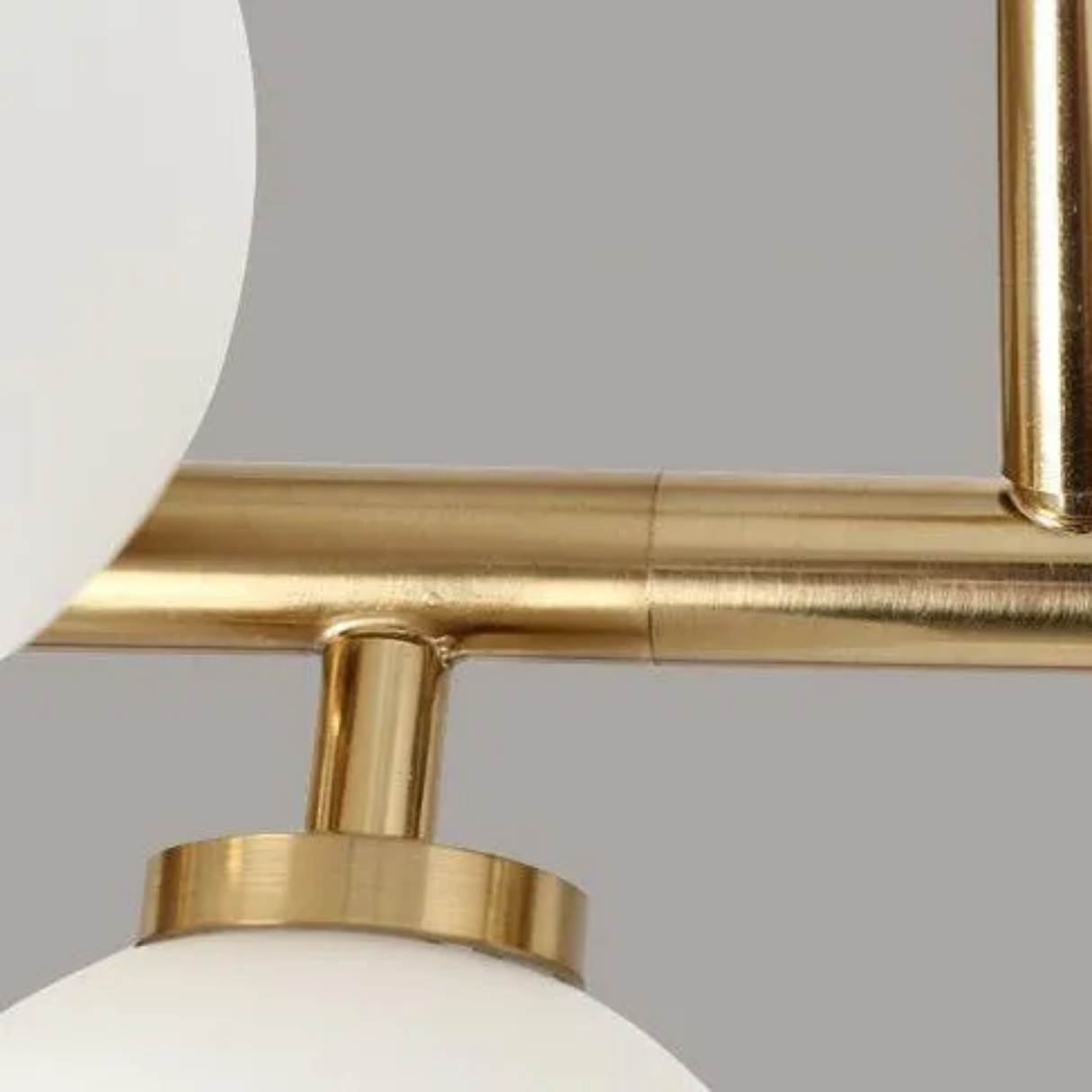 Close-up of a ceiling light fixture with gold finish and white glass on a gray background
