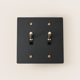 Black switch plate with gold screws on a beige background