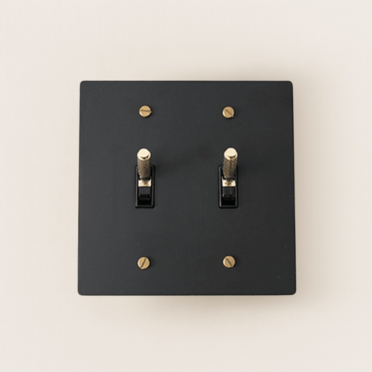 Black switch plate with gold screws on a beige background