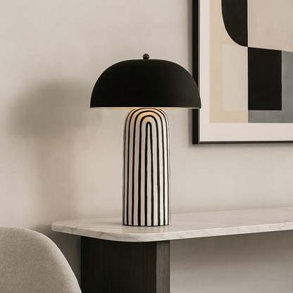 Modern table lamp with black dome shade on a marble surface, abstract art in the background.