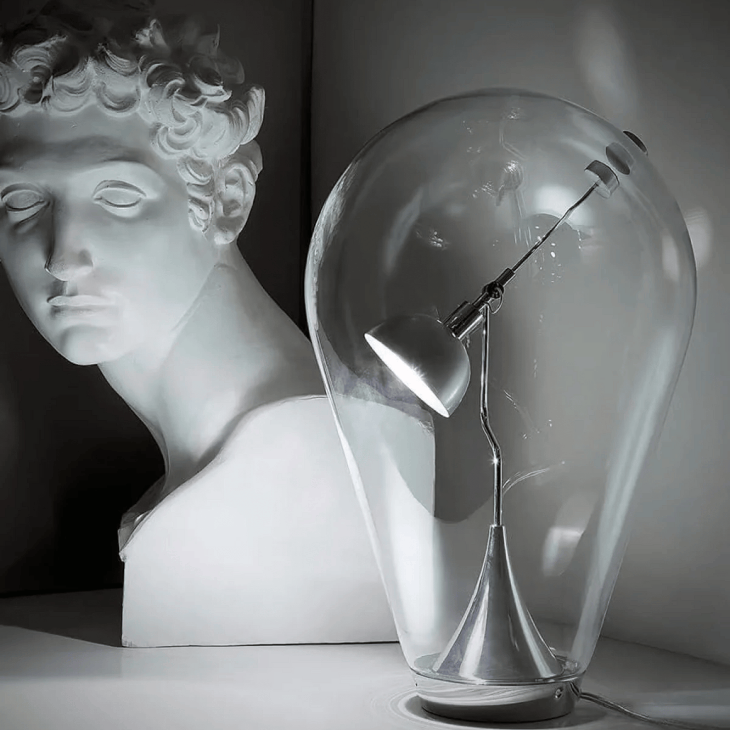 Glass sculpture of a light bulb with a bust in the background