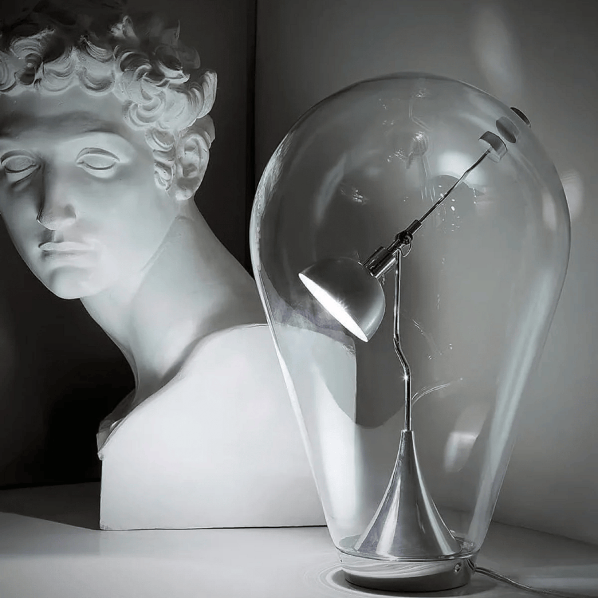 Glass sculpture of a light bulb with a bust in the background