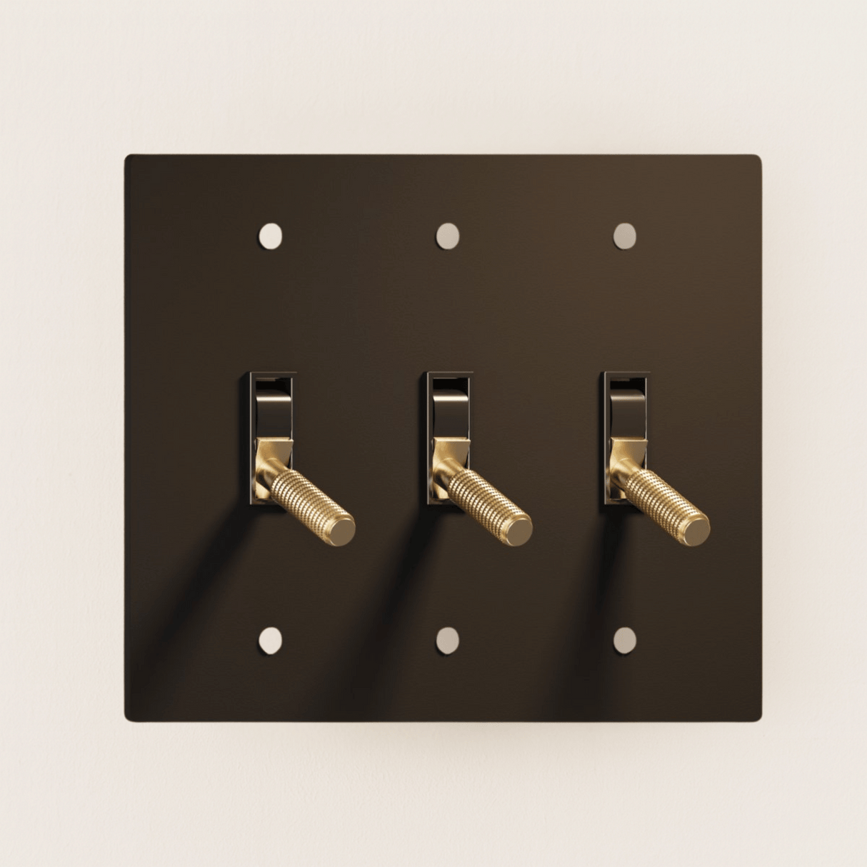 Black wall plate with three gold toggle switches on a beige background