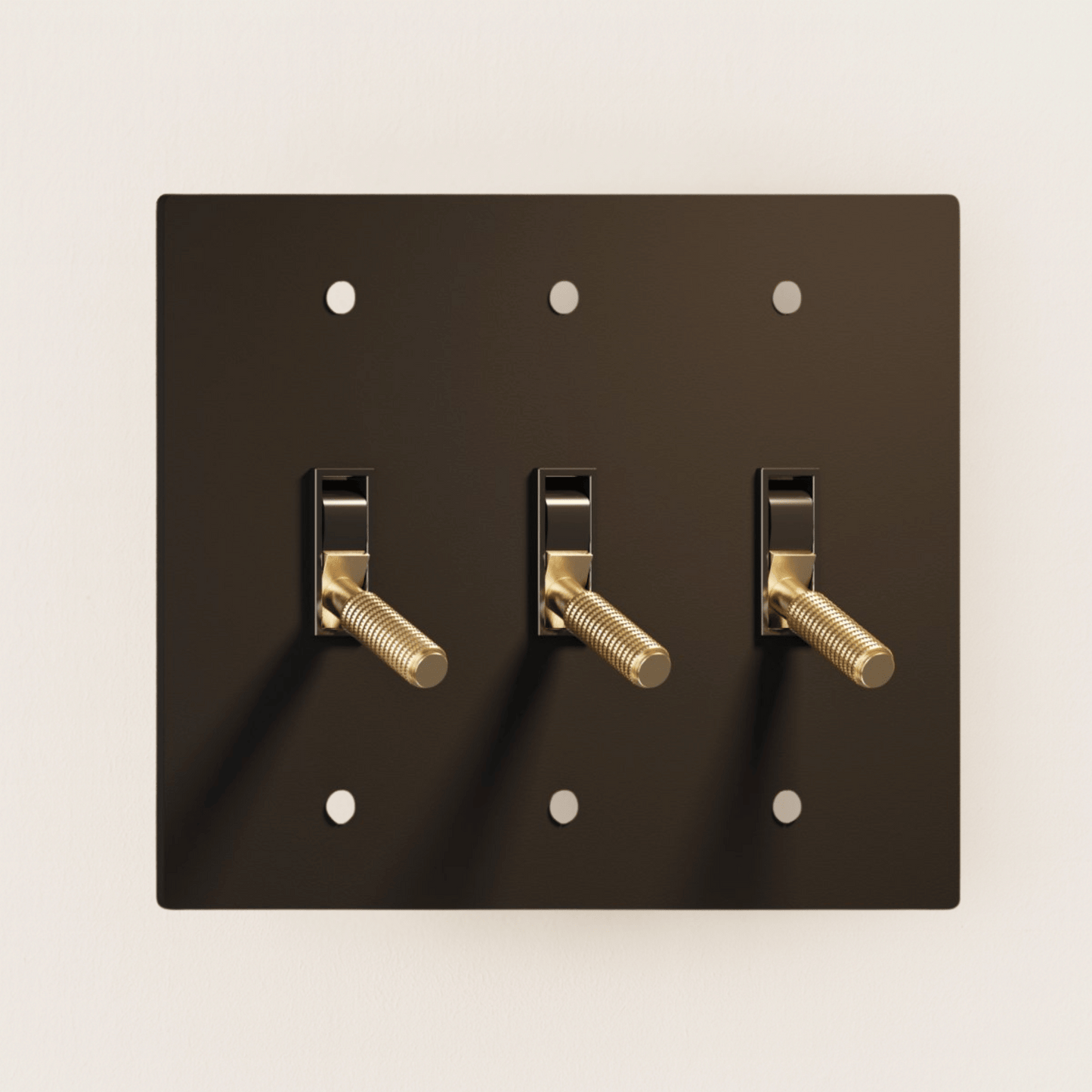 Black wall plate with three gold toggle switches on a beige background