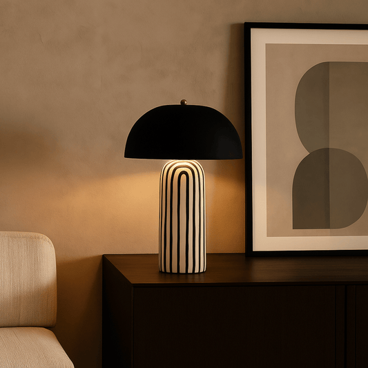 Modern black table lamp with a unique base on a wooden surface, next to abstract art.