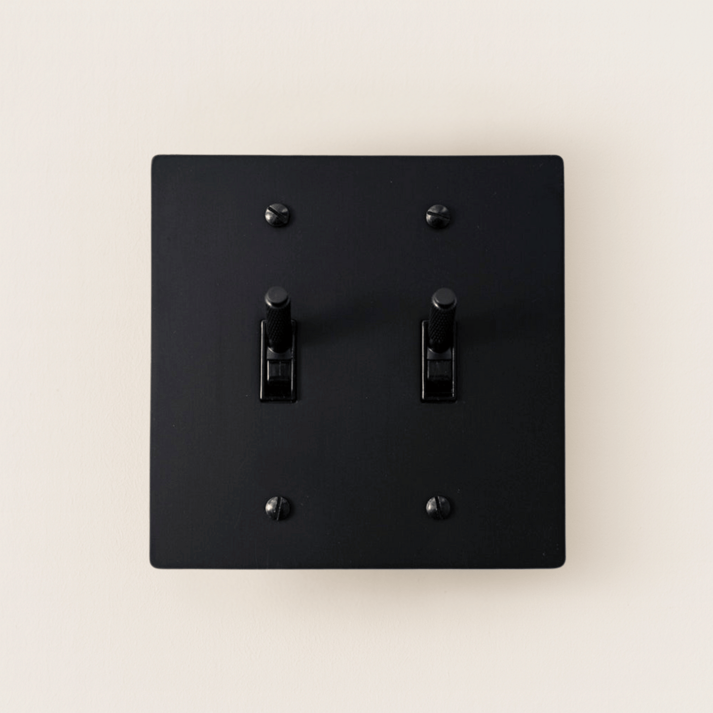Black square light switch with two toggle switches on a beige background