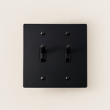Black square light switch with two toggle switches on a beige background