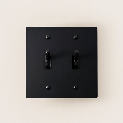 Black square light switch with two toggle switches on a beige background