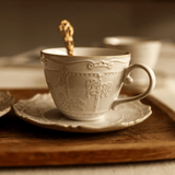 Decorative ceramic cup and saucer with intricate designs on a wooden surface.
