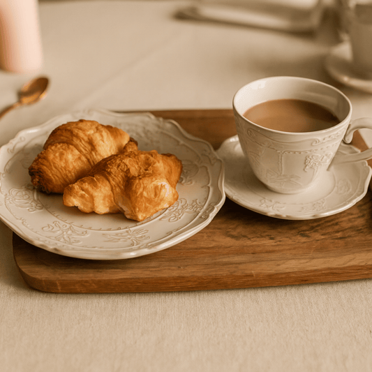 White cup of coffee with a plate of croissants on a wooden tray.