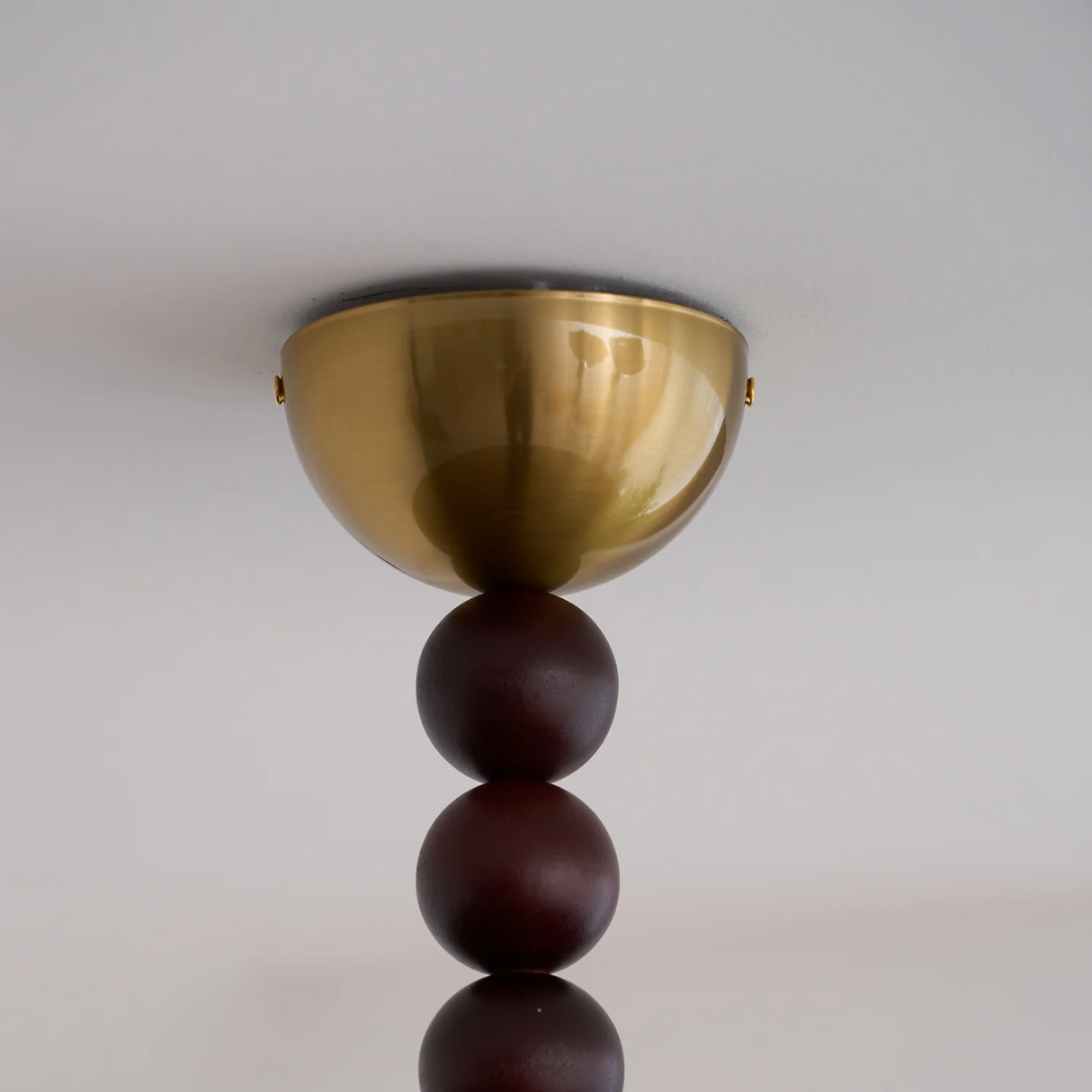 Ceiling light fixture with gold bowl and dark wooden spheres on a plain background