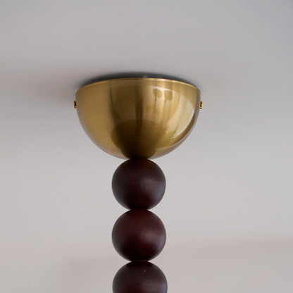 Ceiling light fixture with gold bowl and dark wooden spheres on a plain background