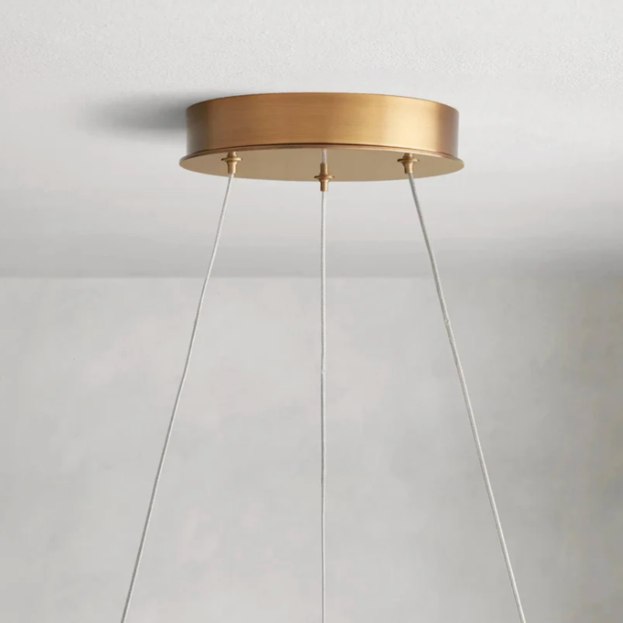 Gold ceiling light fixture with white cables on a plain background