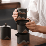 Person holding a stack of black ceramic containers with wavy patterns on a wooden surface.
