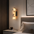 Modern bedroom with wall sconce, books, and a bed with pillows.