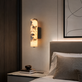 Modern bedroom with wall sconce, books, and a bed with pillows.