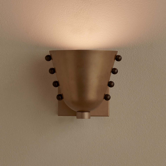 Bronze wall sconce with decorative elements on a beige wall