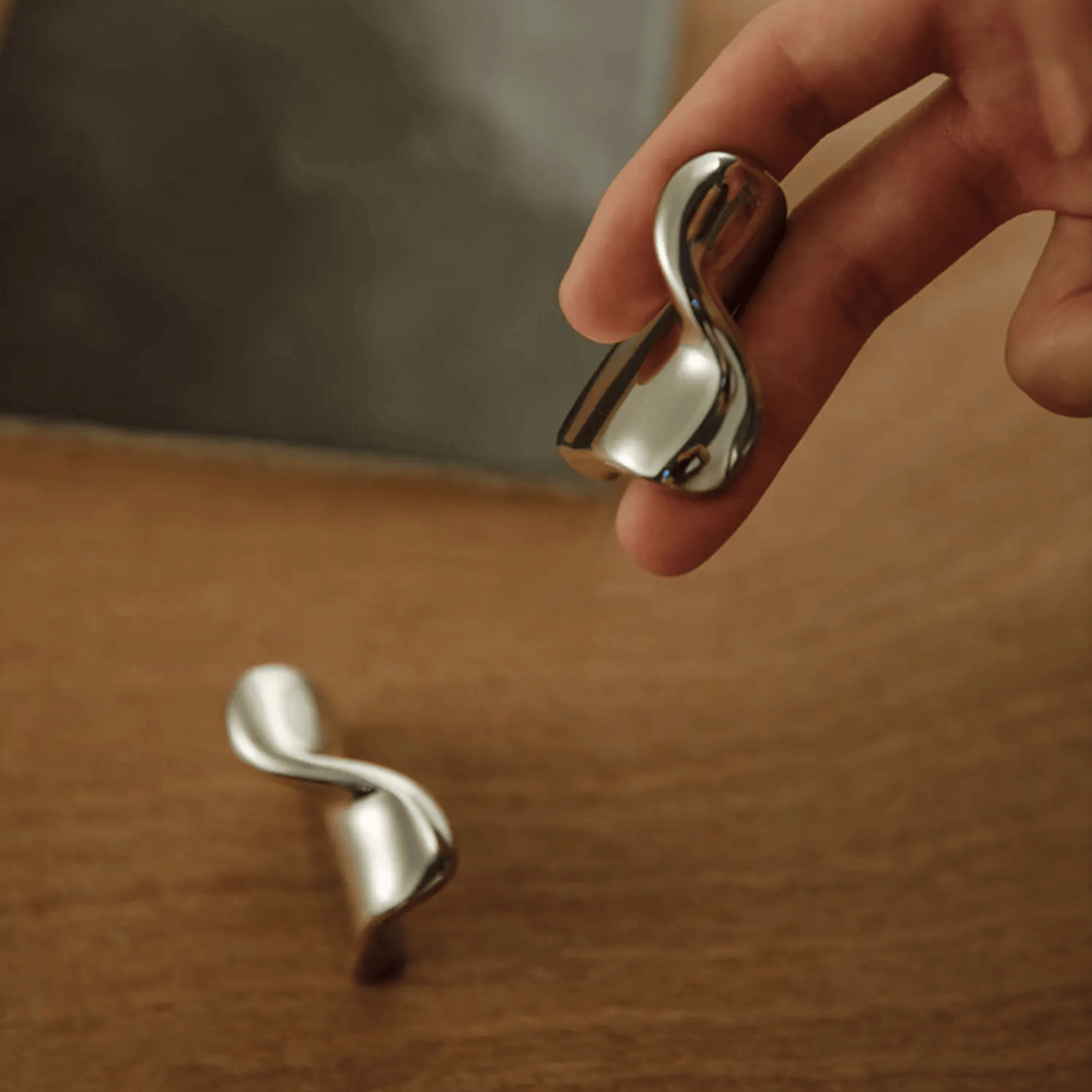 Silver earrings with a wavy design held by a hand on a wooden surface.