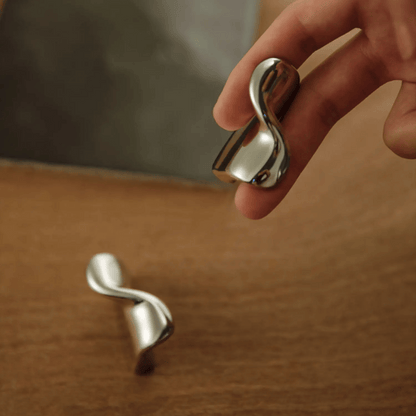 Silver earrings with a wavy design held by a hand on a wooden surface.