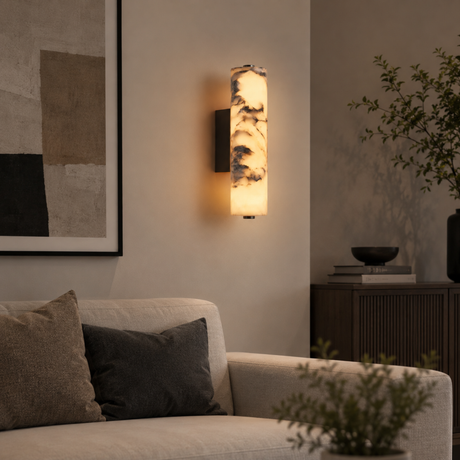 Wall-mounted cylindrical light fixture in a living room setting with a couch and decorative items.
