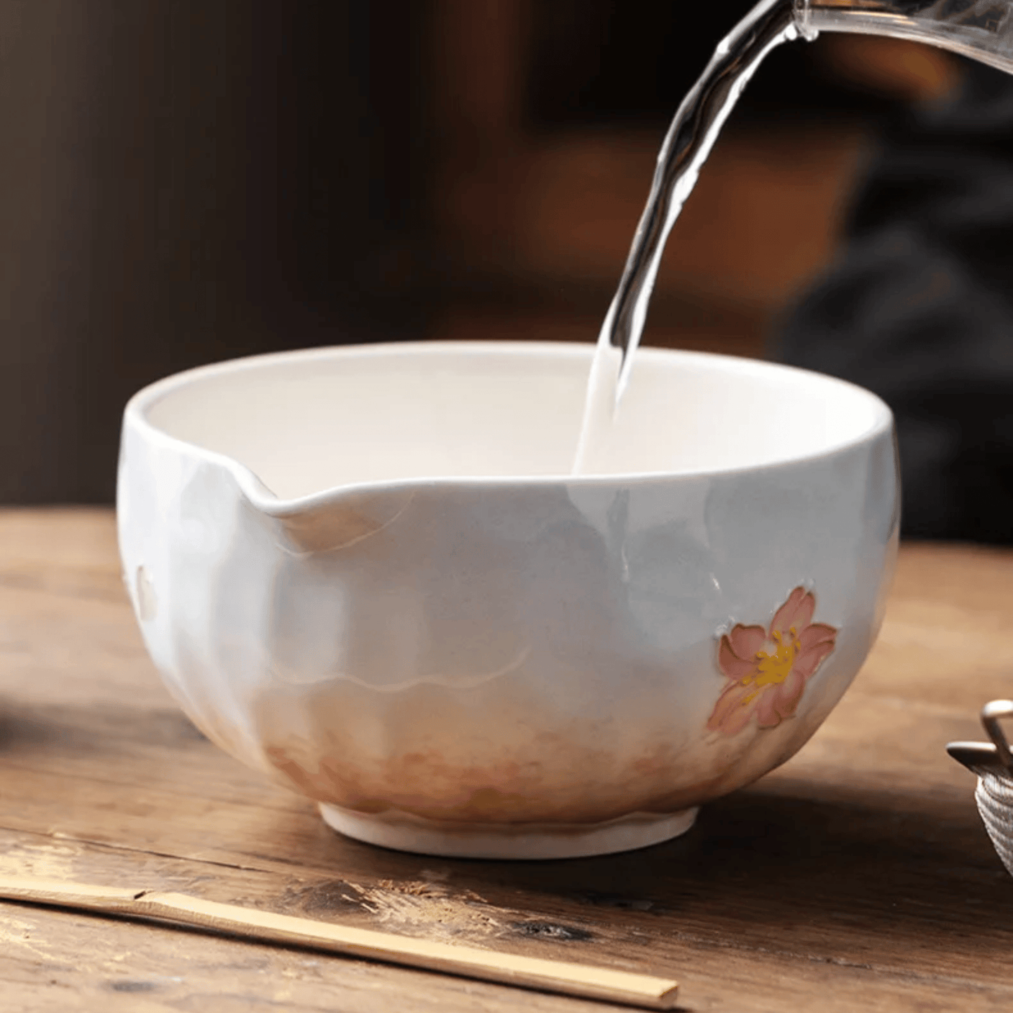 White ceramic teacup with floral design being filled with water on a wooden surface.
