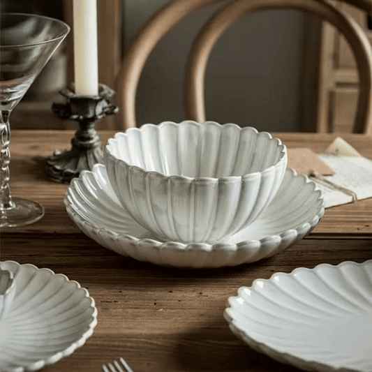 Decorative white ceramic bowl on a wooden table with a candle and glass in the background.