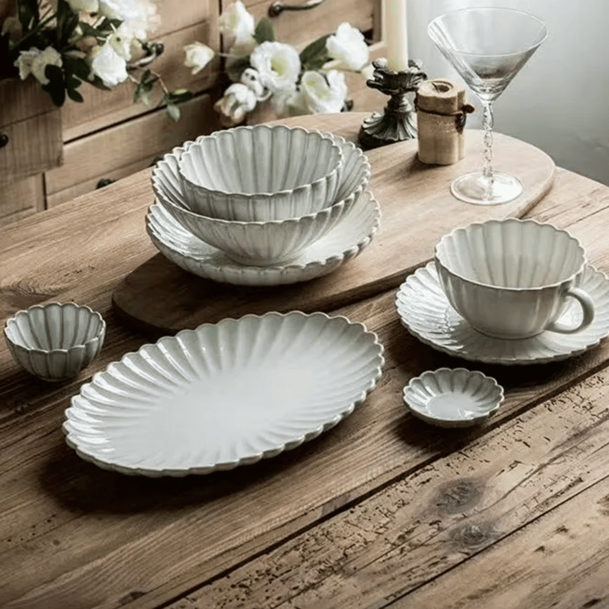 Set of ceramic dishes on a wooden table with flowers and a candle in the background