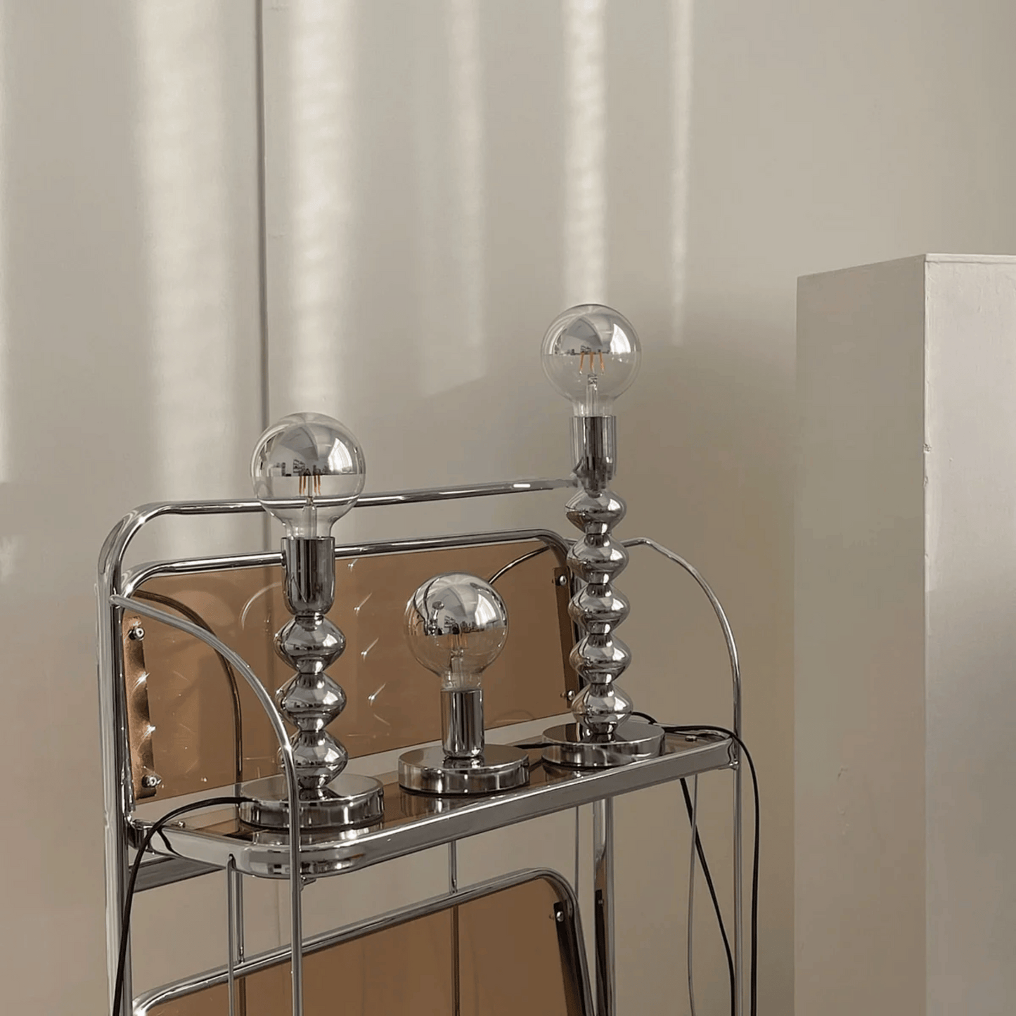 Chrome bar cart with three glass light bulbs on a neutral background